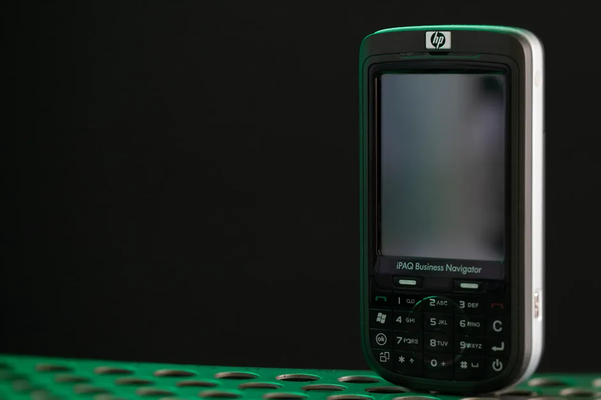 Close-up of a vintage HP iPAQ Business Navigator mobile device on a perforated surface.