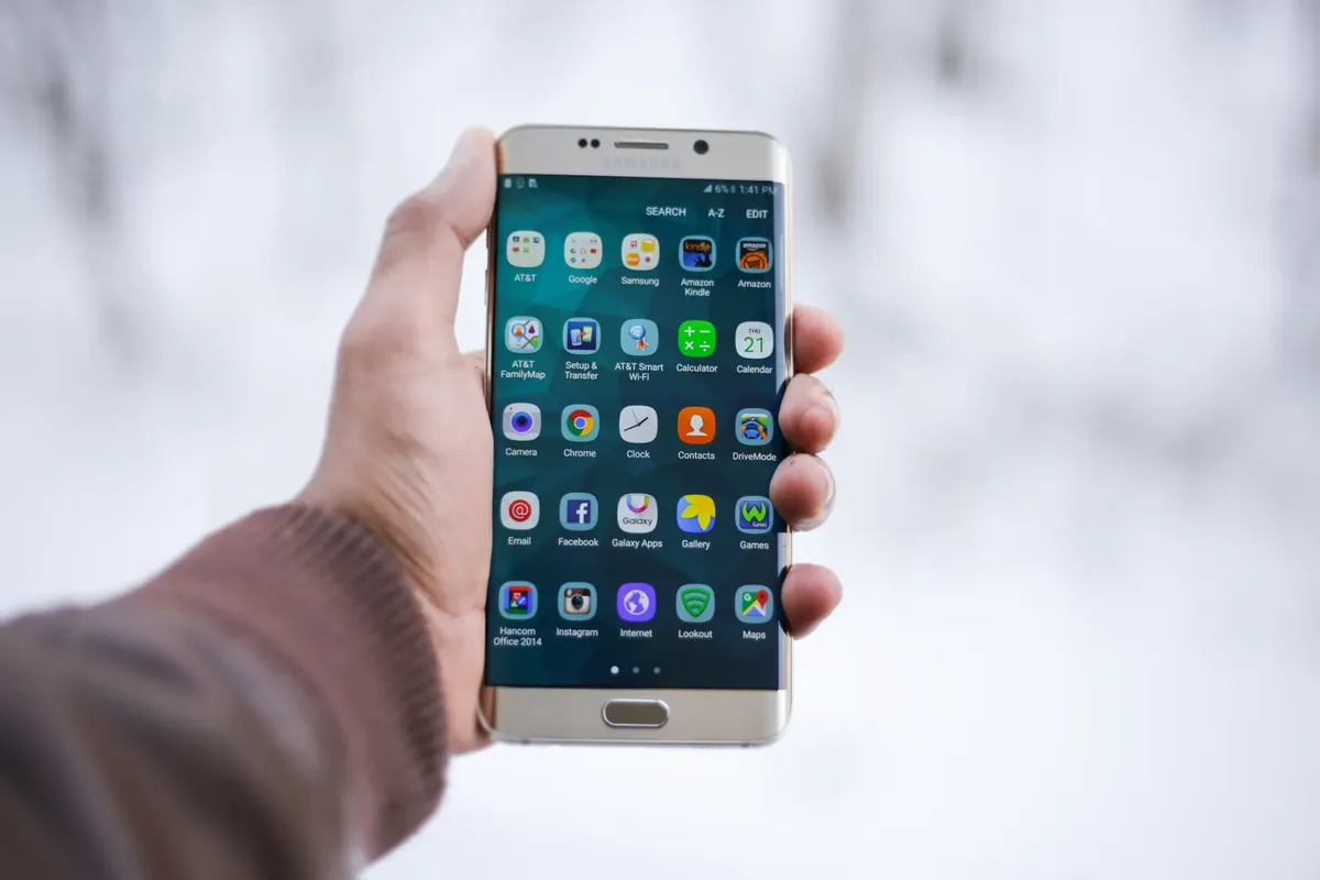 手がサムスンスマートフォンを握り、さまざまなアプリアイコンが表示されているクローズアップ。技術と接続性を強調。