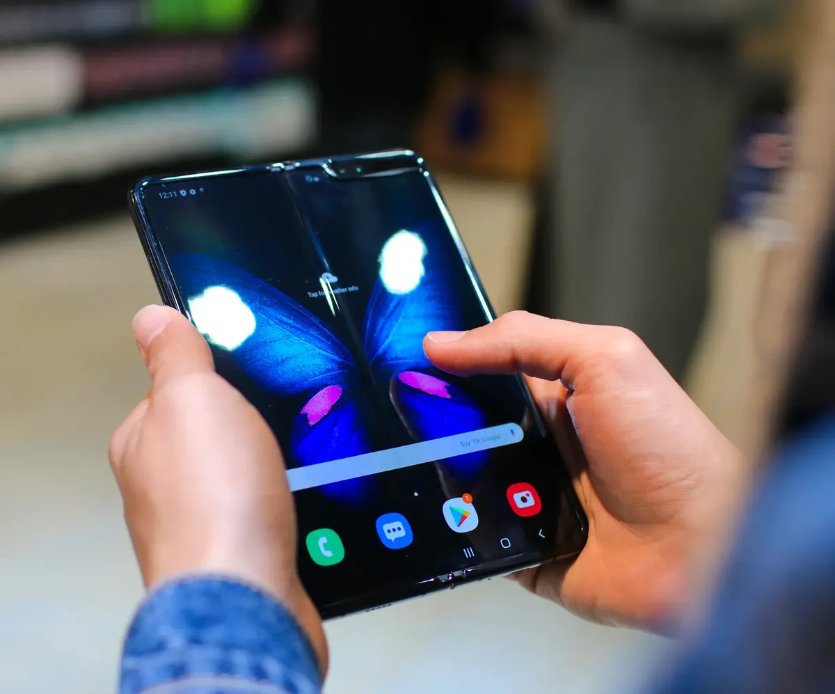 Close-up of hands holding a foldable smartphone showing a butterfly on the screen.