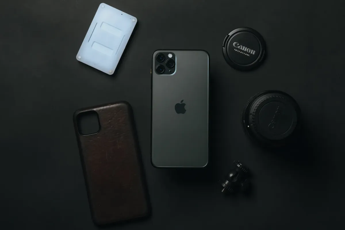 From above of expensive smartphone placed near camera lens and phone case on dark table